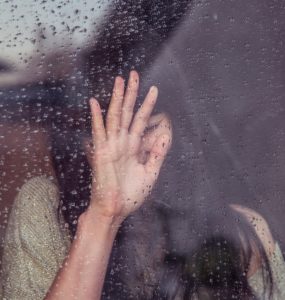 Depressed young woman behind rain covered window.